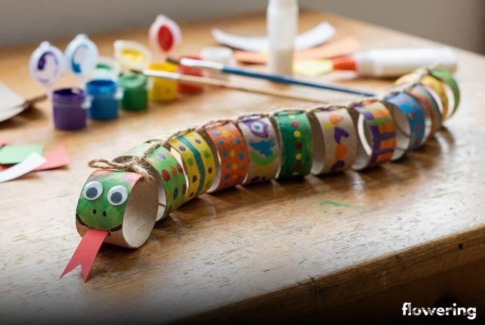 Kolorowy wąż z połączonych rolek po papierze toaletowym, z papierowym językiem i oczami, ułożony falą na blacie