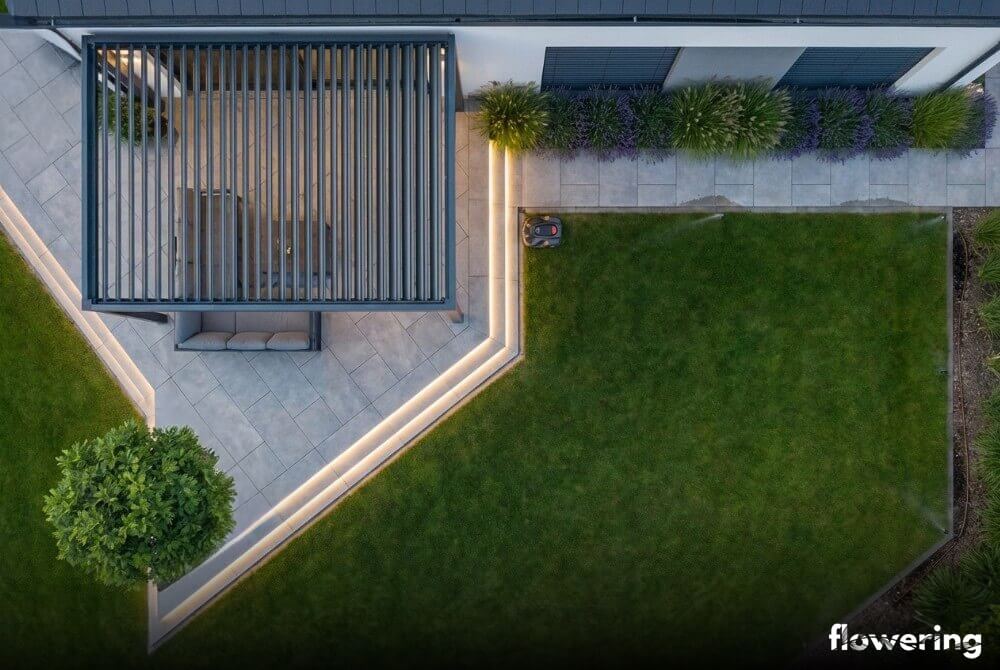 Widok z góry Smart Garden przy domu z pergolą bioklimatyczną, geometrycznym tarasem, liniowym oświetleniem LED, trawnikiem oraz uporządkowanymi nasadzeniami lawendy i trzcinnika